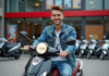 Jeune homme souriant avec scooter en ville